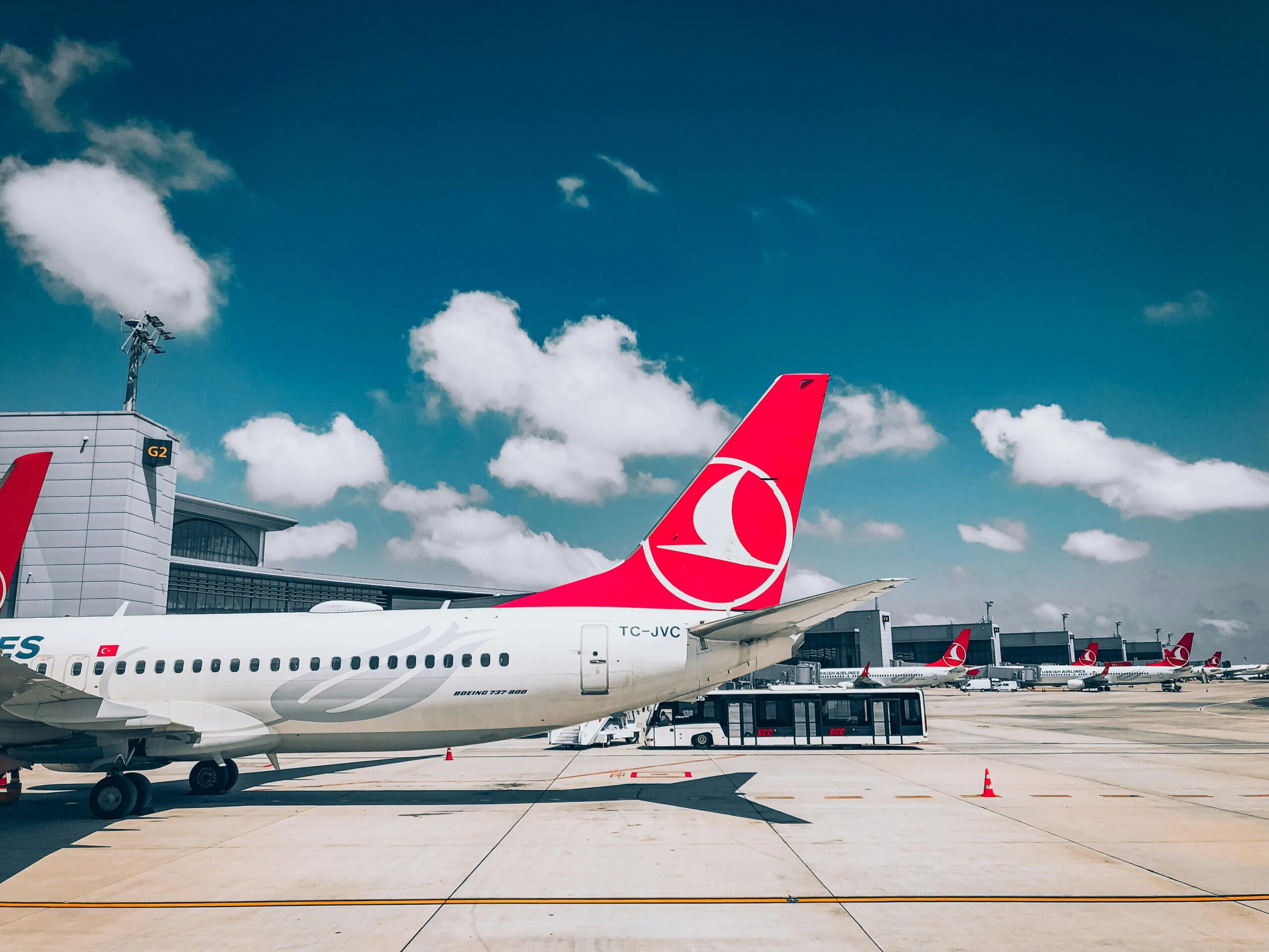 Airplanes on a tarmac at an airport with red tail logos, clear blue sky, and scattered clouds.